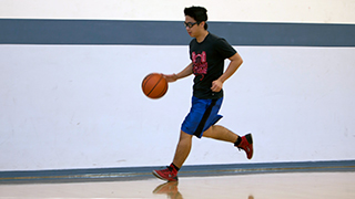 A student is dribbling a basketball on the NMT practice court.
